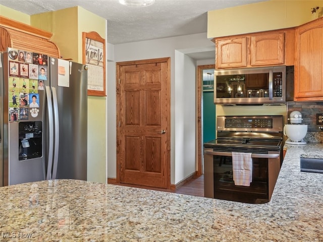 kitchen featuring light stone countertops, a textured ceiling, and appliances with stainless steel finishes