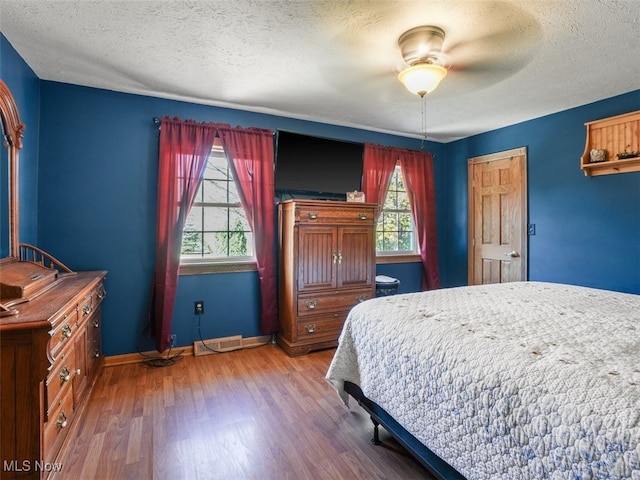 bedroom with hardwood / wood-style floors, ceiling fan, a textured ceiling, and multiple windows