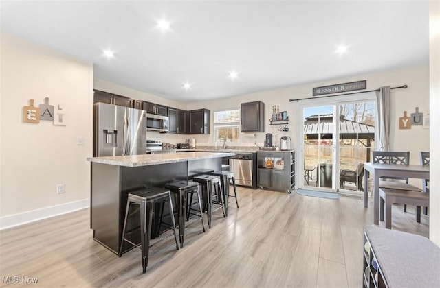 kitchen featuring a center island, a kitchen breakfast bar, light hardwood / wood-style flooring, dark brown cabinets, and stainless steel appliances