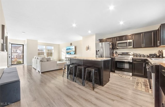 kitchen with a breakfast bar, light wood-type flooring, appliances with stainless steel finishes, dark brown cabinets, and a kitchen island