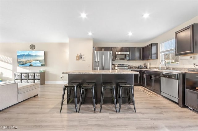 kitchen with light stone countertops, stainless steel appliances, a breakfast bar area, a kitchen island, and light wood-type flooring