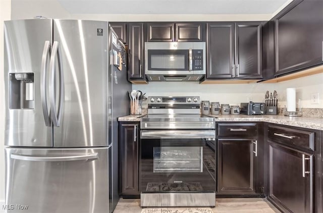 kitchen featuring dark brown cabinetry, light stone countertops, light hardwood / wood-style flooring, and appliances with stainless steel finishes