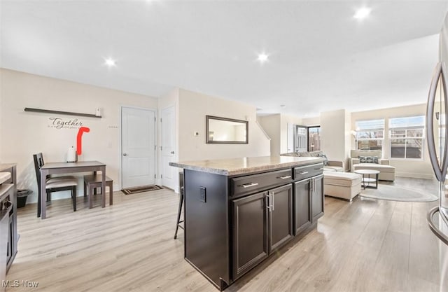 kitchen featuring a center island, light hardwood / wood-style flooring, light stone counters, a kitchen bar, and dark brown cabinetry