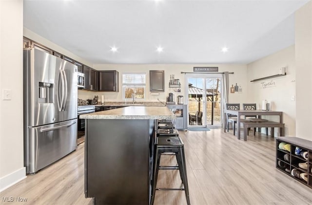 kitchen featuring a breakfast bar, dark brown cabinetry, stainless steel appliances, a center island, and light hardwood / wood-style floors