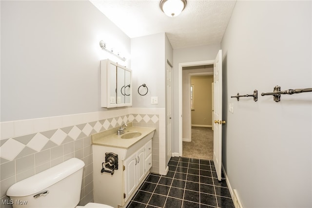 bathroom with a textured ceiling, vanity, toilet, and tile walls