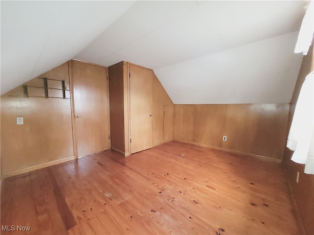 additional living space featuring light wood-type flooring, wooden walls, and lofted ceiling