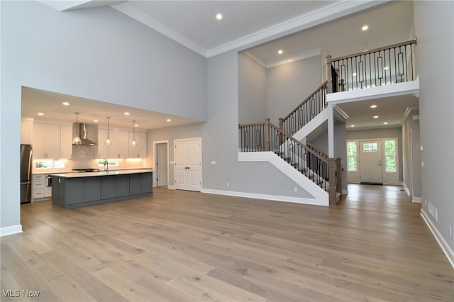 unfurnished living room featuring a towering ceiling, light wood-type flooring, and ornamental molding