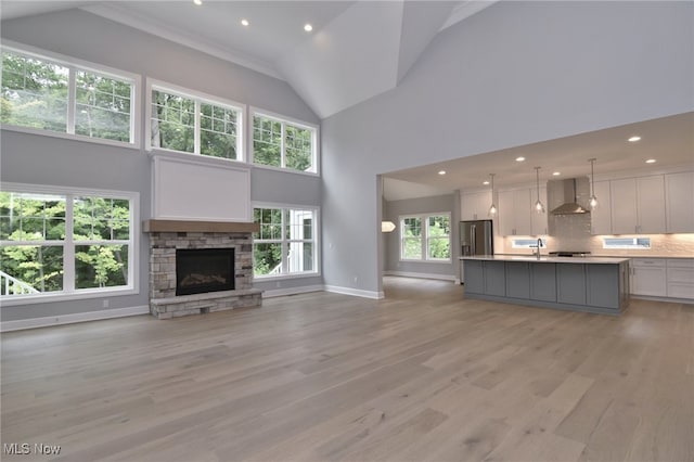 unfurnished living room with a stone fireplace, sink, high vaulted ceiling, and light hardwood / wood-style flooring