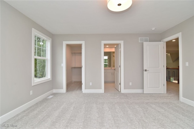 unfurnished bedroom featuring a closet, light colored carpet, a spacious closet, and ensuite bath