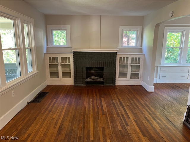 unfurnished living room with dark wood-type flooring and a brick fireplace