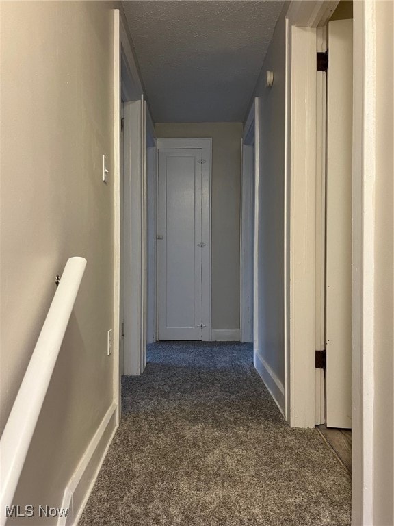 hall featuring dark carpet and a textured ceiling