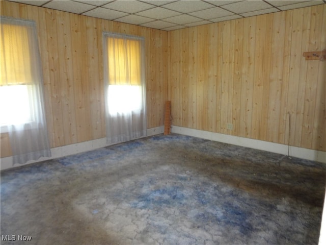 empty room featuring wood walls, a drop ceiling, and carpet floors