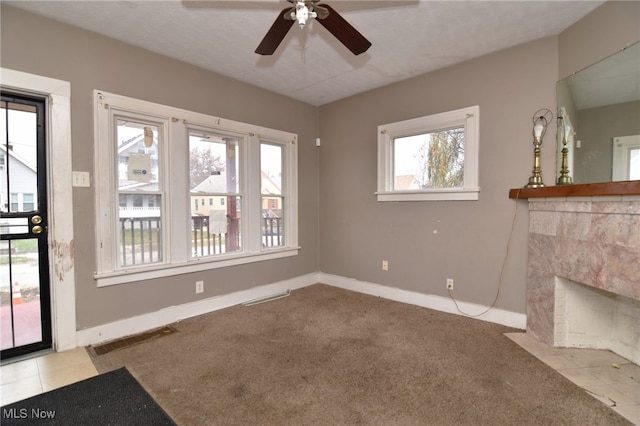 unfurnished living room with a tile fireplace, light carpet, ceiling fan, and a textured ceiling