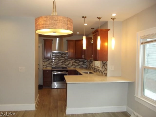 kitchen with sink, wall chimney exhaust hood, stainless steel electric range oven, decorative light fixtures, and kitchen peninsula