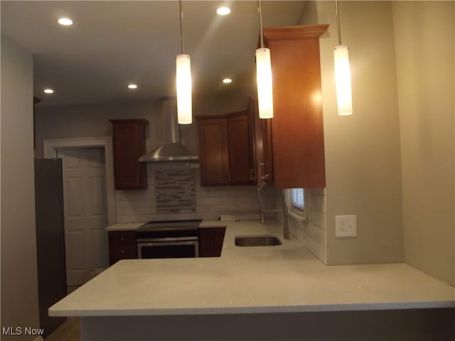 kitchen with wall chimney exhaust hood, kitchen peninsula, fridge, decorative light fixtures, and decorative backsplash