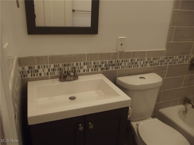 bathroom featuring vanity, a bath, tile walls, and toilet