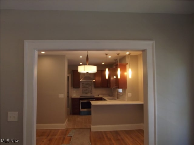 kitchen featuring exhaust hood, stainless steel electric stove, decorative backsplash, decorative light fixtures, and light hardwood / wood-style floors