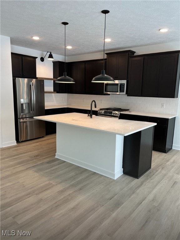 kitchen with decorative light fixtures, stainless steel appliances, a kitchen island with sink, and light hardwood / wood-style floors