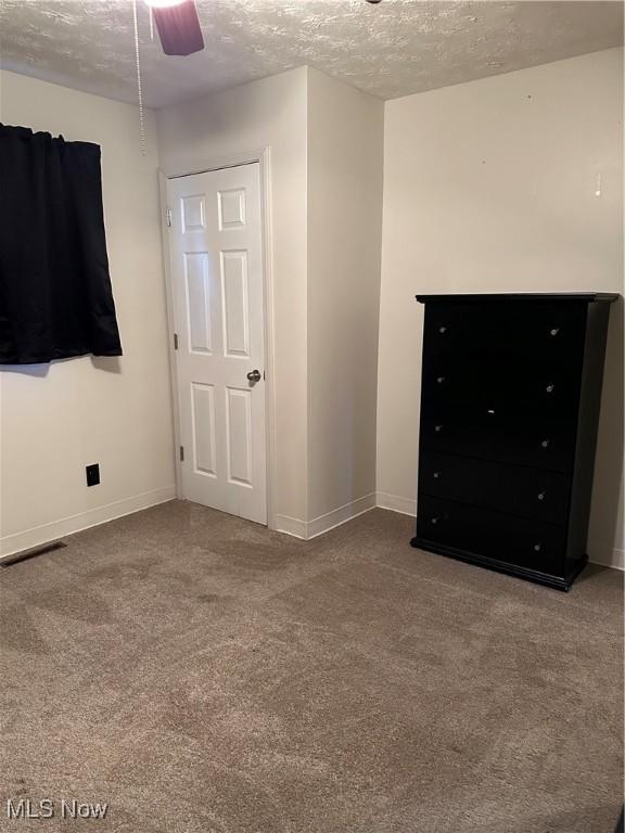 unfurnished bedroom featuring carpet, a textured ceiling, and ceiling fan