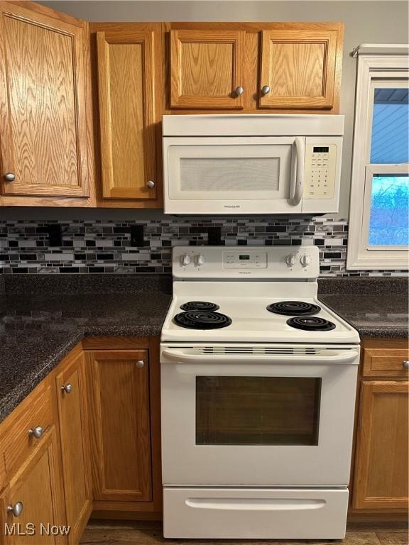 kitchen with dark stone countertops, white appliances, and tasteful backsplash