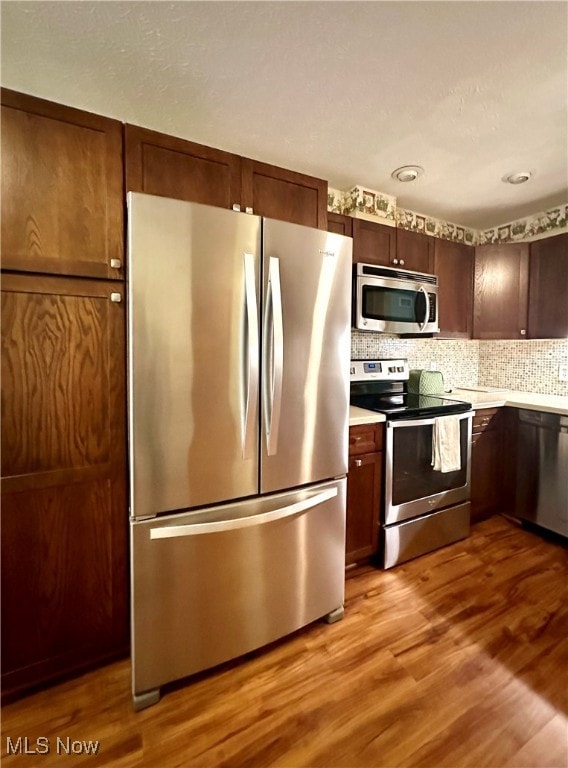 kitchen with appliances with stainless steel finishes, light hardwood / wood-style floors, and tasteful backsplash