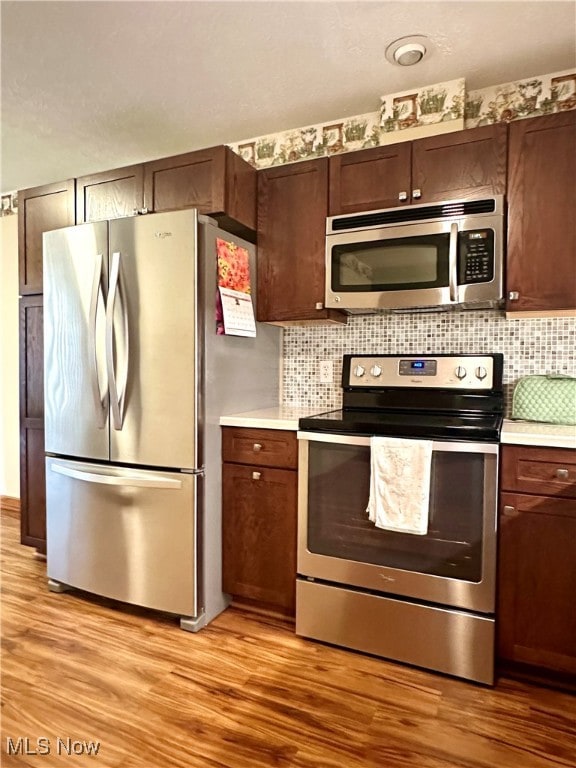 kitchen featuring backsplash, dark brown cabinetry, light wood-type flooring, and stainless steel appliances