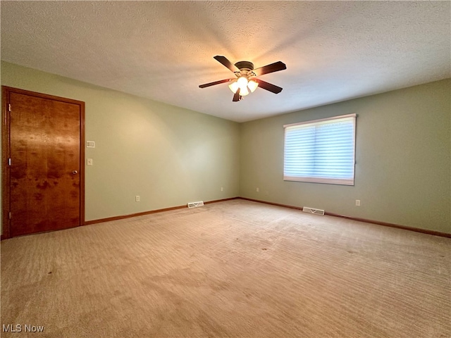 empty room featuring ceiling fan, light colored carpet, and a textured ceiling