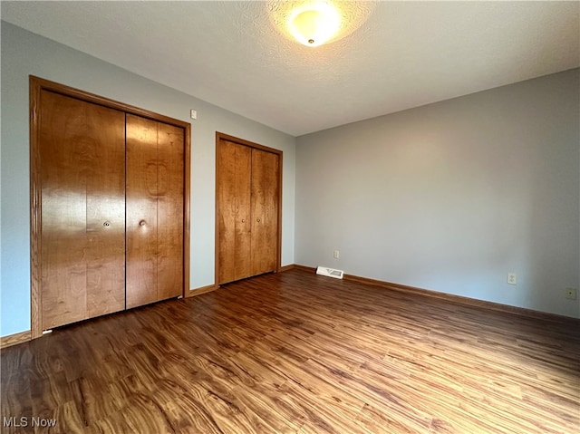 unfurnished bedroom featuring multiple closets, hardwood / wood-style floors, and a textured ceiling