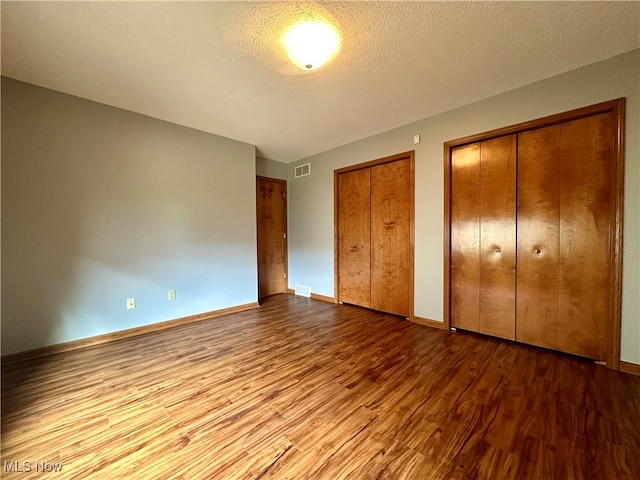 unfurnished bedroom featuring multiple closets, wood-type flooring, and a textured ceiling