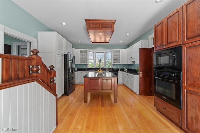 kitchen with a center island, black appliances, a kitchen breakfast bar, light hardwood / wood-style flooring, and white cabinetry