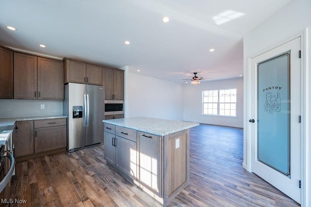 kitchen with light stone countertops, appliances with stainless steel finishes, ceiling fan, dark hardwood / wood-style floors, and a kitchen island