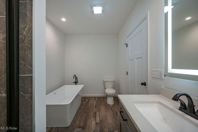 bathroom featuring hardwood / wood-style floors, vanity, a bath, and toilet