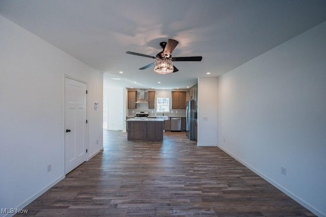 kitchen with ceiling fan, a center island, wall chimney exhaust hood, stainless steel appliances, and dark hardwood / wood-style flooring