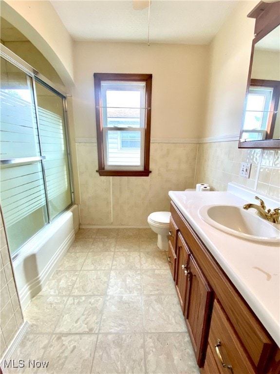 full bathroom with toilet, vanity, tile walls, and shower / bath combination with glass door