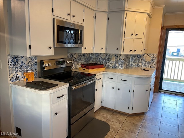 kitchen with white cabinets, ornamental molding, light tile patterned floors, tasteful backsplash, and stainless steel appliances