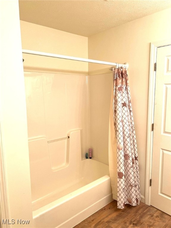 bathroom with hardwood / wood-style floors, shower / bathtub combination with curtain, and a textured ceiling