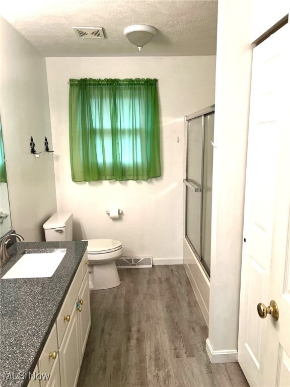 full bathroom with combined bath / shower with glass door, a textured ceiling, toilet, vanity, and hardwood / wood-style flooring