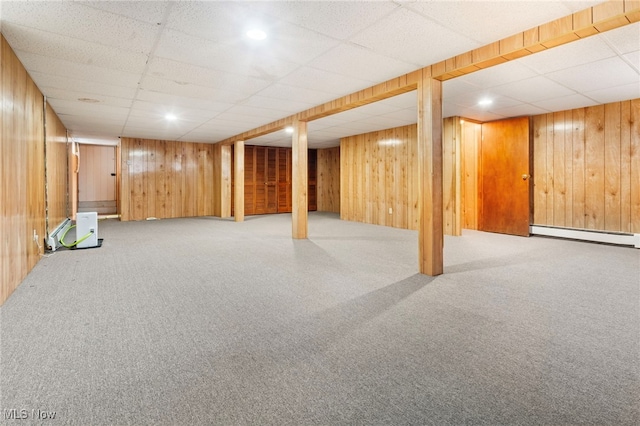 basement featuring a drop ceiling, wood walls, and baseboard heating