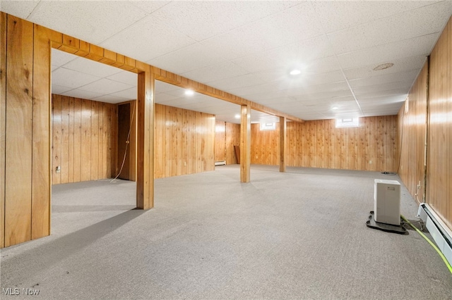 basement with a drop ceiling, light colored carpet, baseboard heating, and wooden walls