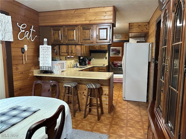 kitchen with kitchen peninsula, a kitchen bar, white appliances, wooden walls, and light parquet flooring