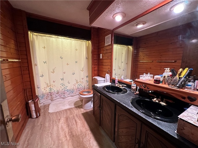 bathroom featuring wood walls, hardwood / wood-style floors, a textured ceiling, toilet, and vanity