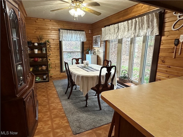 dining area with wooden walls, light parquet floors, a textured ceiling, and ceiling fan