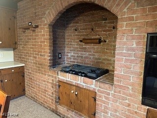 kitchen with black gas stovetop, light colored carpet, and brick wall