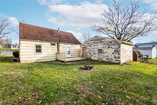 rear view of house featuring a storage shed, a wooden deck, a fire pit, central AC unit, and a lawn