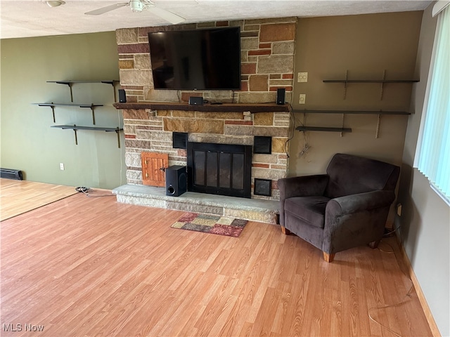 living room with a textured ceiling, ceiling fan, wood-type flooring, and a fireplace