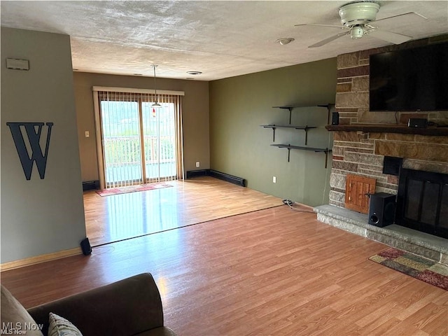 living room with a textured ceiling, light hardwood / wood-style flooring, ceiling fan, and a stone fireplace