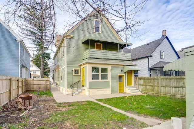 rear view of house featuring a balcony and a lawn