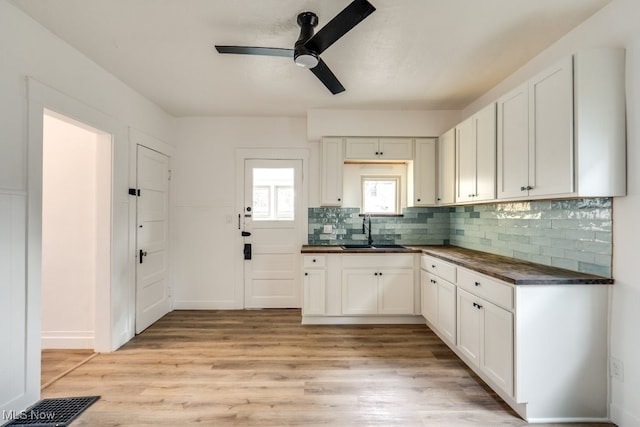 kitchen with white cabinets, light wood-type flooring, backsplash, and sink