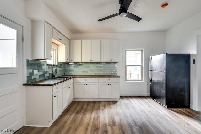 kitchen featuring backsplash, white cabinets, black fridge, sink, and light wood-type flooring