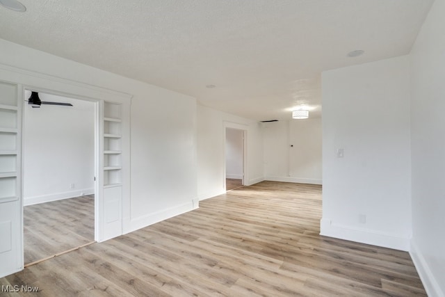 spare room with built in features, a textured ceiling, and light hardwood / wood-style flooring